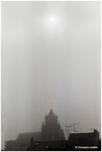 Photo noir et blanc de la galerie " Esotérisme". Eglise Saint Gervais-Saint Protais  de Gisors ( XII ème siècle) avec son clocher sous la brume et la percée de l'astre solaire. © Mars 2005 Christophe Letellier, tous droits réservés. Pour revenir à la galerie, cliquez sur la photo.