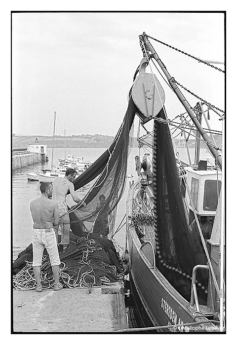 Photo noir et blanc "Douarnenez, le port du Rosmeur" dans le Finistère-Dans le Port Rosmeur de Douarnenez, des pêcheurs vident la cargaison du grand filet de pêche de leut bateau de pêche.© Juillet 2006 Christophe Letellier tous droits réservés.