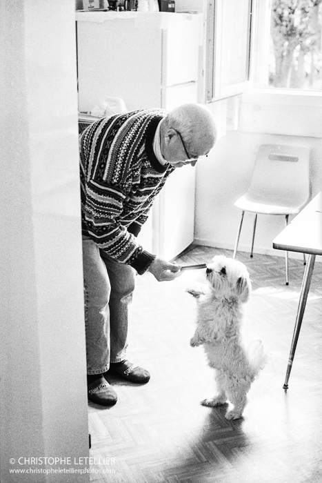 Photo en noir et blanc d'un vieil homme donnant une barre de nourriture à son bichon maltais © 2016 Christophe Letellier all rights reserved. 